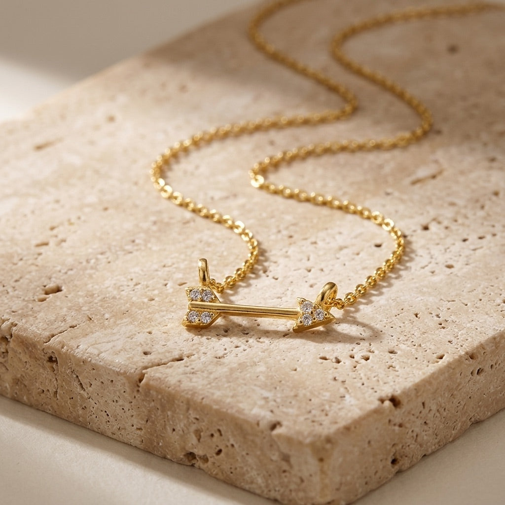 Gold necklace with an arrow pendant on a textured stone surface