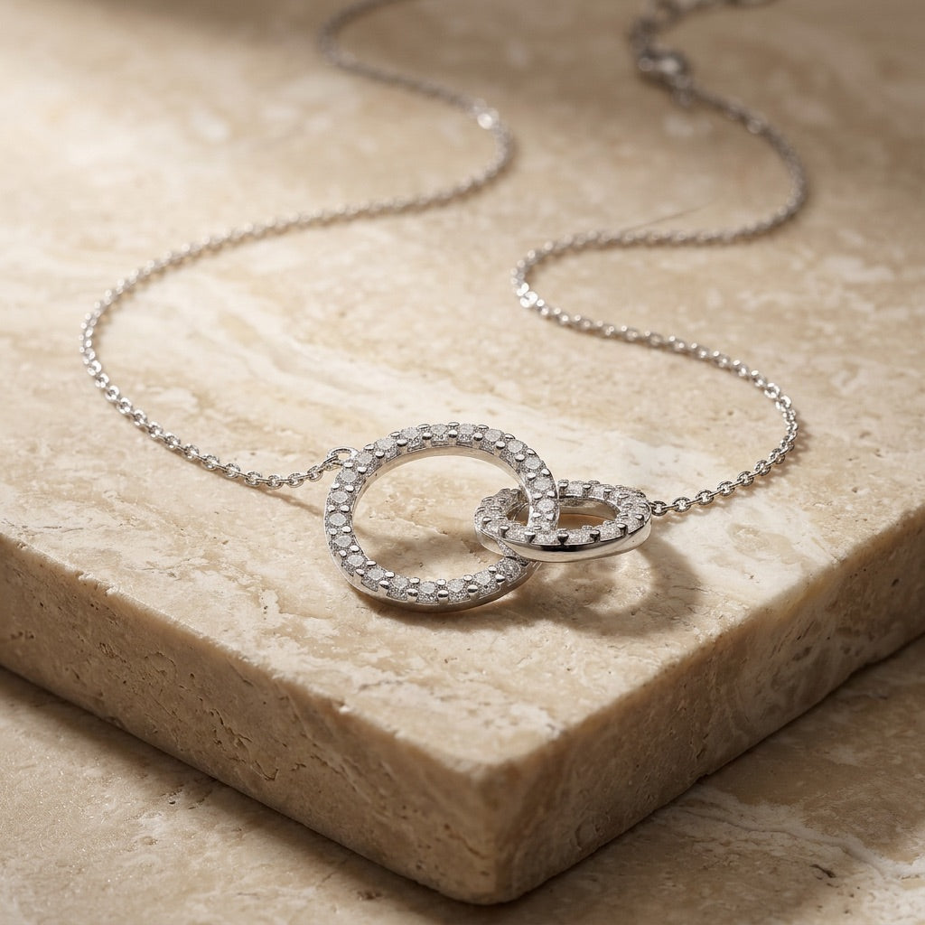 Silver necklace with interlocking rings on a beige stone surface