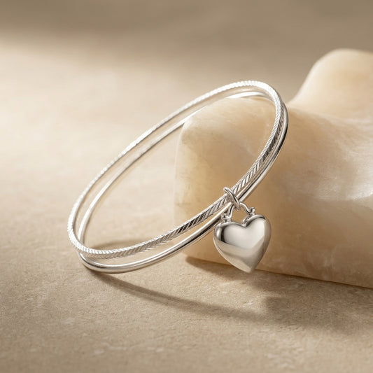 Silver bangle with a heart-shaped charm on a beige background