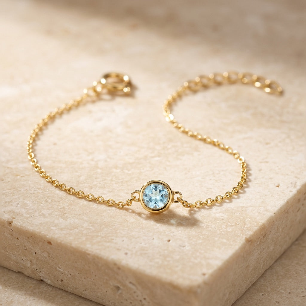 Gold bracelet with a blue gemstone on a beige stone surface