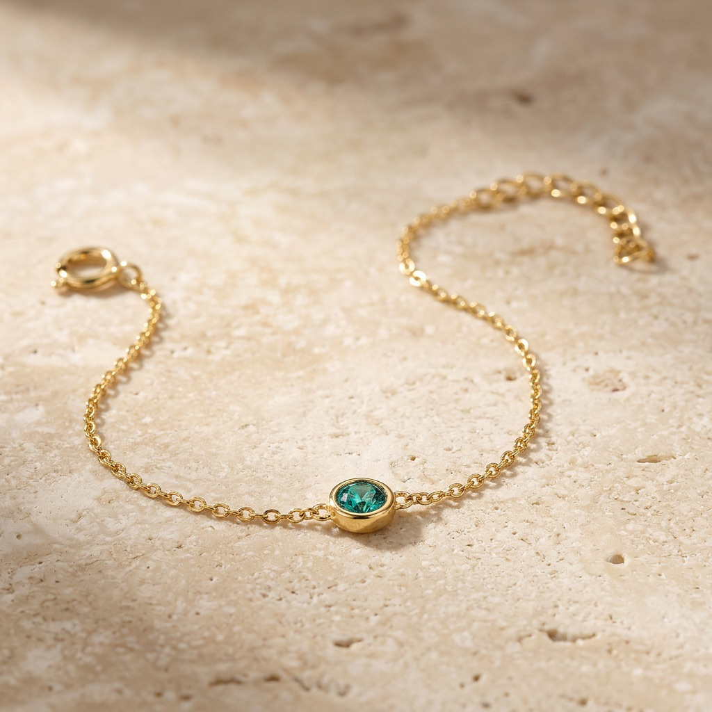 Gold bracelet with a green gemstone on a beige stone surface