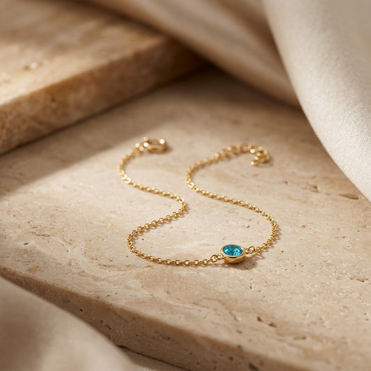 Gold bracelet with a blue gemstone on a beige stone surface