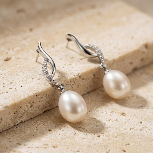 Pearl earrings with silver hooks on a beige stone surface