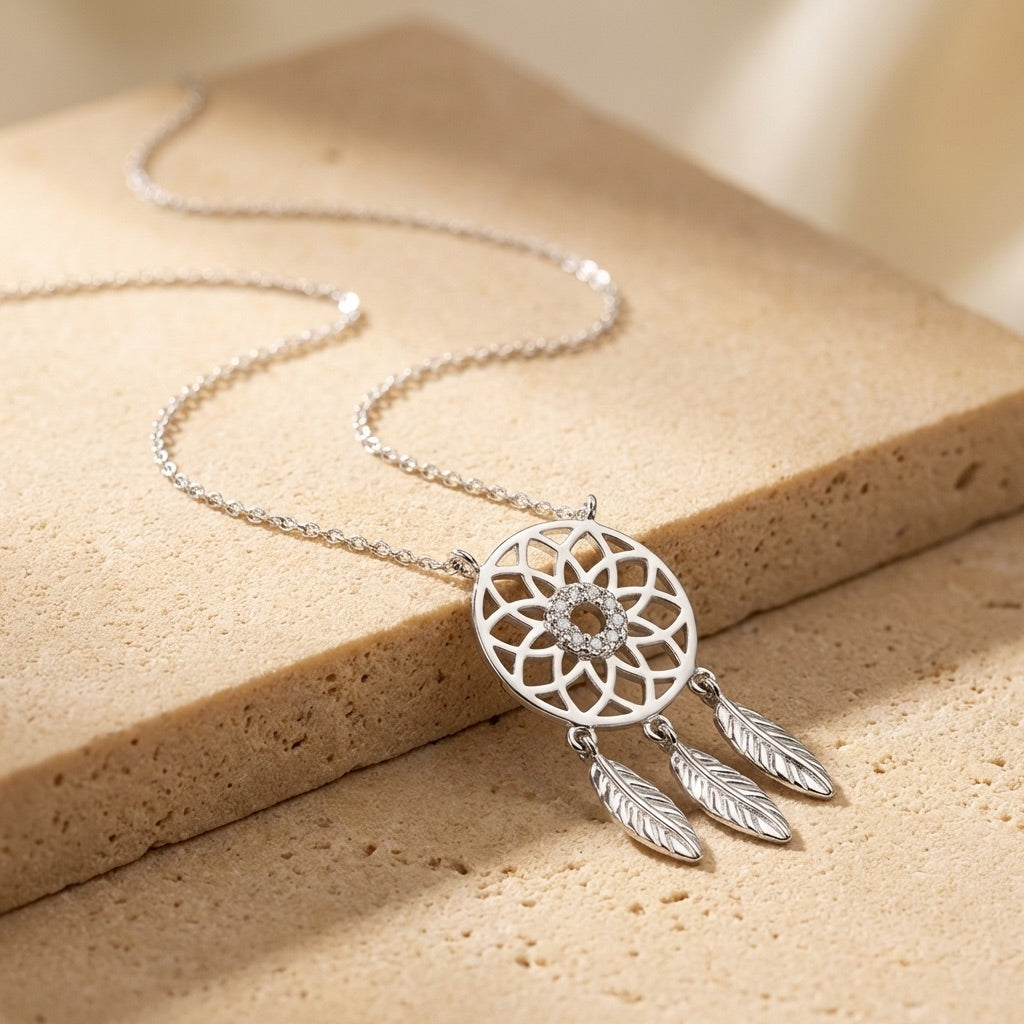 Silver dreamcatcher necklace on a beige stone surface