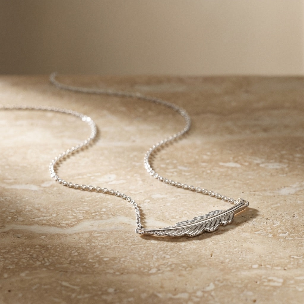 Silver feather necklace on a beige surface
