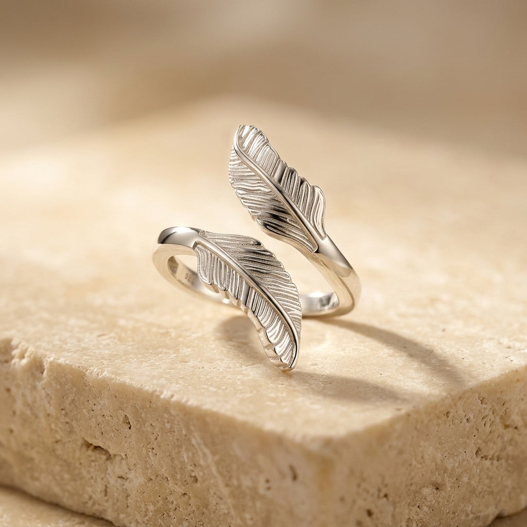 Silver feather-shaped ring on a beige stone surface