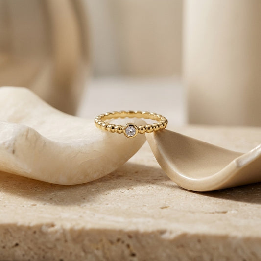Gold ring with a diamond on a beige stone surface