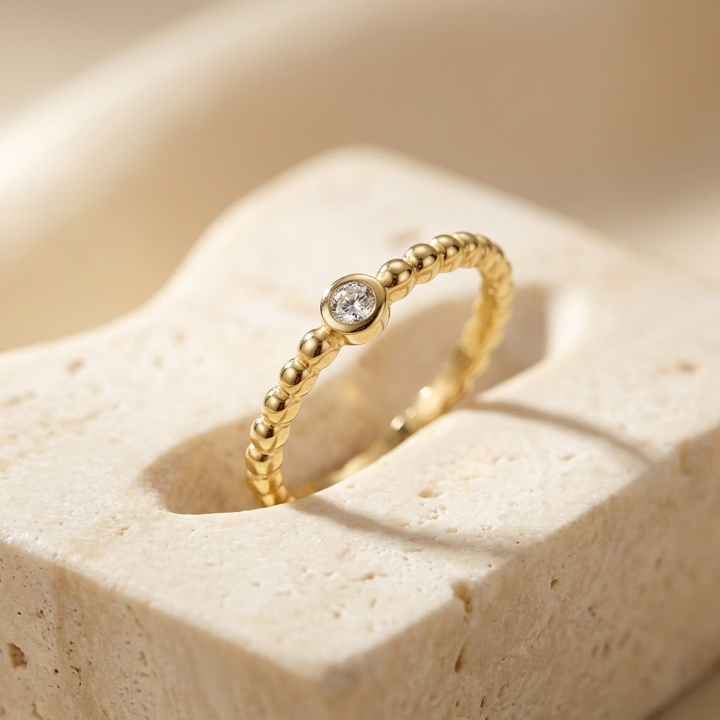 Gold ring with a diamond on a beige stone surface