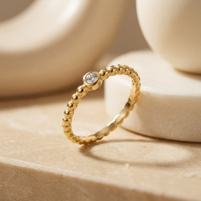 Gold ring with a diamond on a beige surface