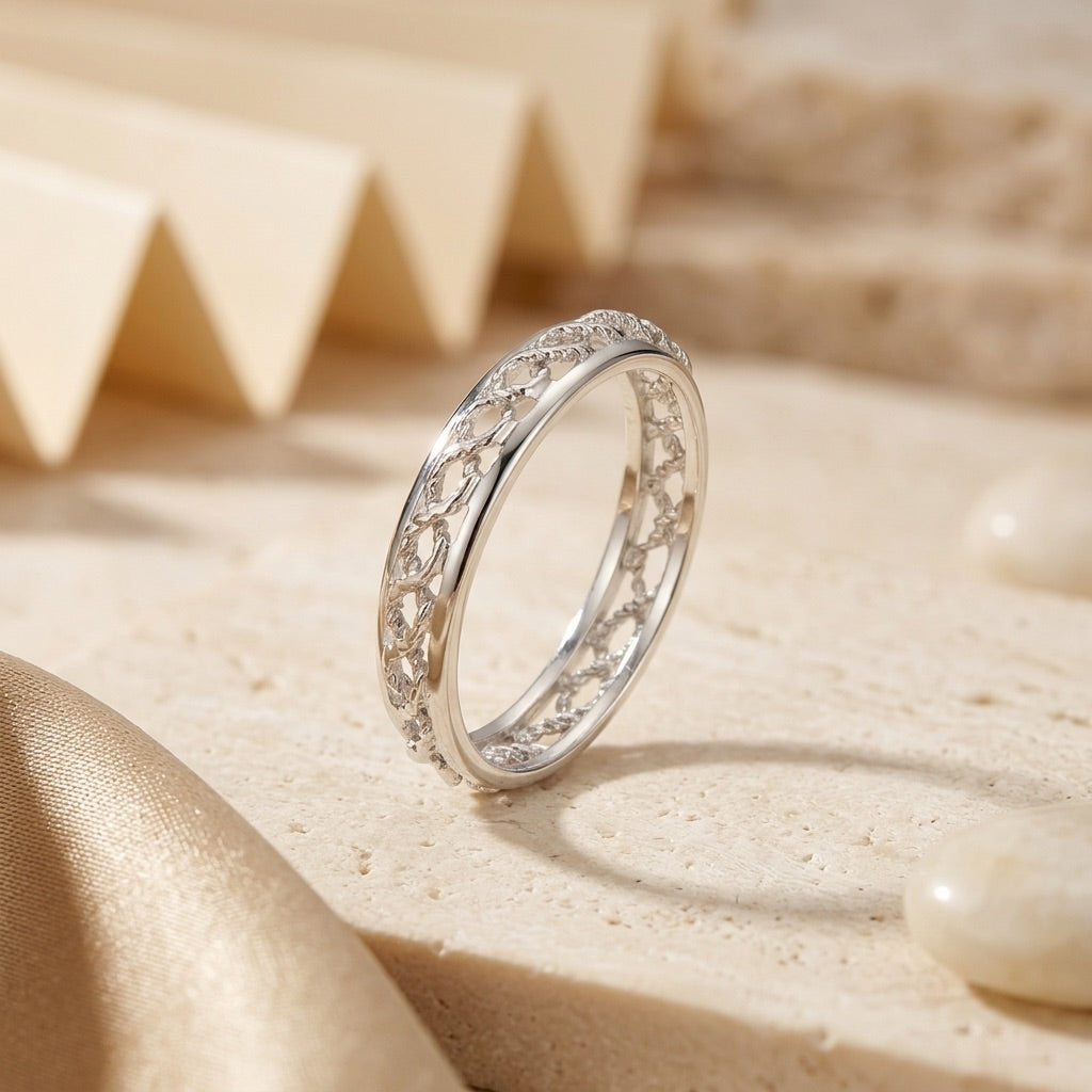 Silver ring with intricate design on a beige sand-like surface