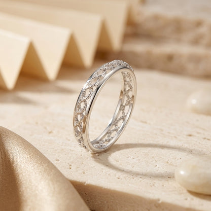 Silver ring with intricate design on a beige sand-like surface