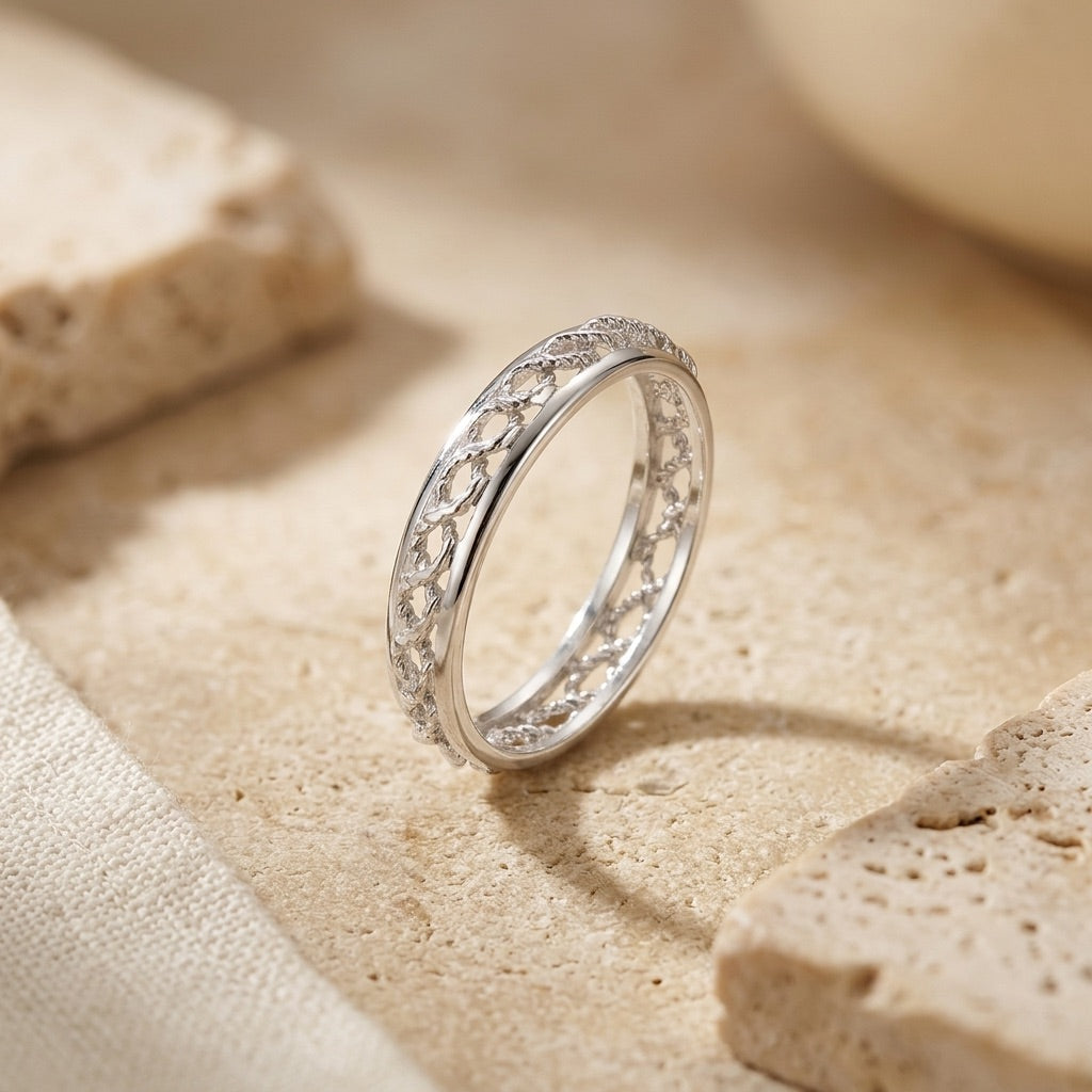 Silver ring with intricate design on a sandy surface