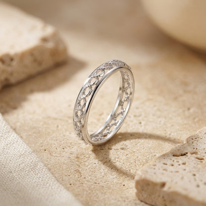 Silver ring with intricate design on a sandy surface