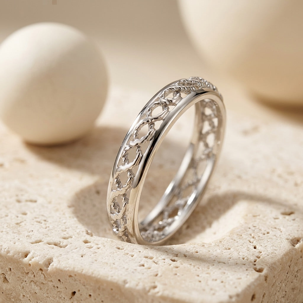 Silver ring with intricate design on a sandy surface