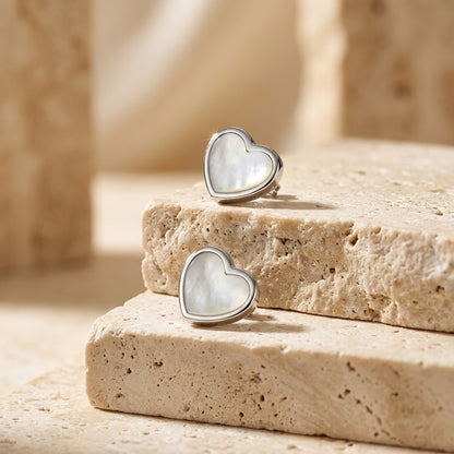 Spectrum Dinky White Mother of Pearl Heart Stud Earrings on a stone surface with a blurred natural background