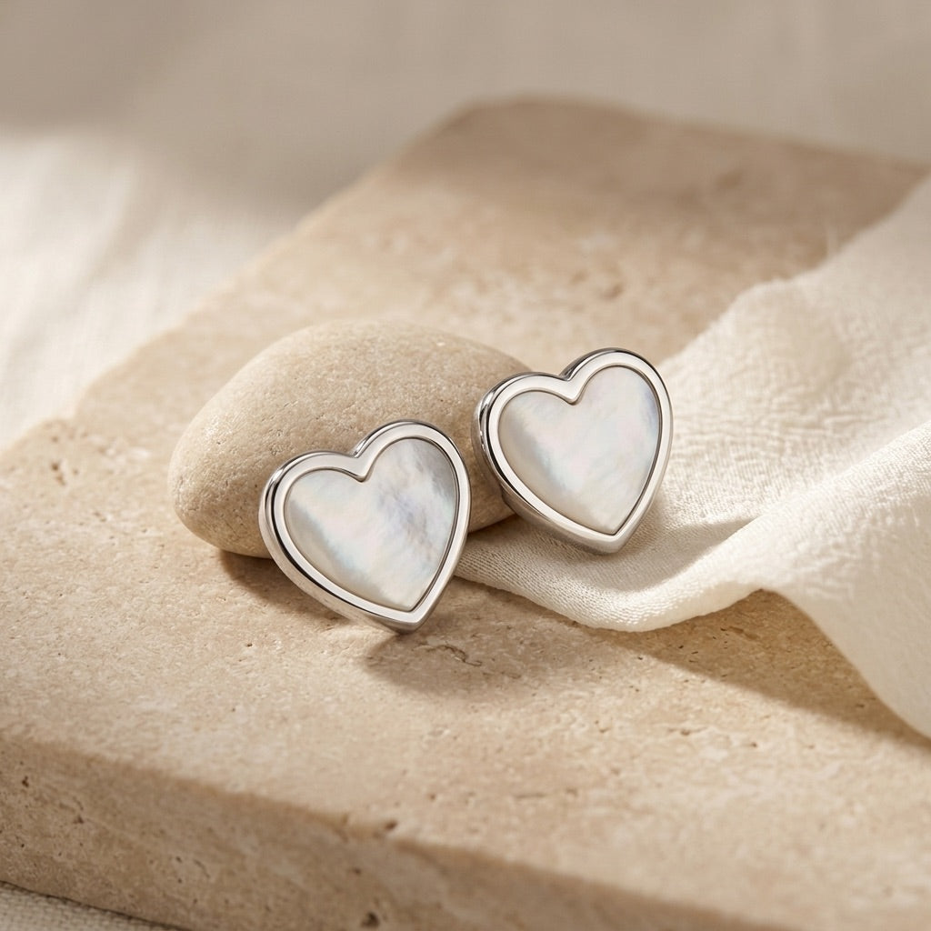 Heart-shaped earrings with a mother-of-pearl finish on a beige stone surface