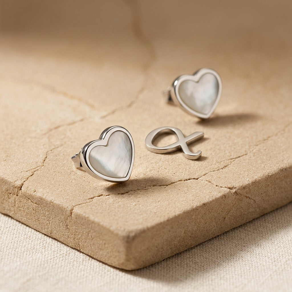 Spectrum Dinky White Mother of Pearl Heart Stud Earrings on a textured beige surface