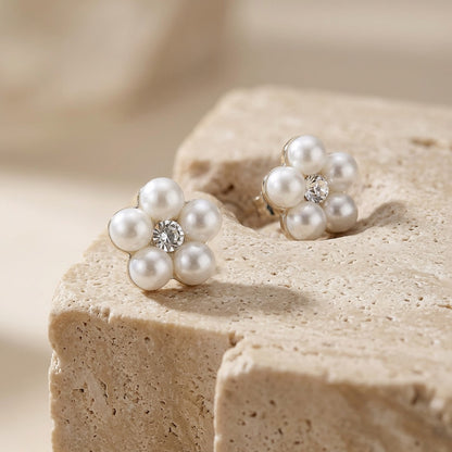 Pearl flower earrings with a central gemstone on a beige stone surface