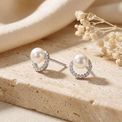 Pearl earrings with silver circular designs on a beige stone surface with dried flowers.