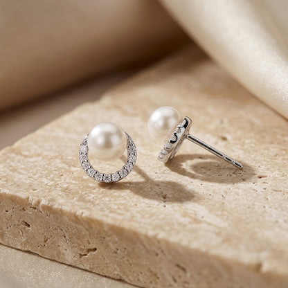 Pearl earrings with silver posts on a textured beige surface