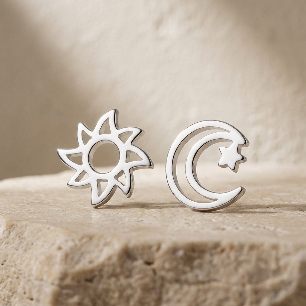 Silver sun and moon and star earrings on a beige stone surface