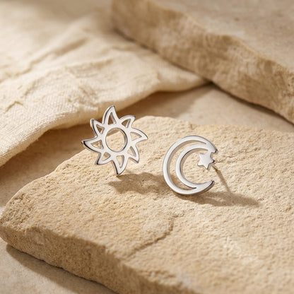 Silver sun and moon earrings on a beige stone surface