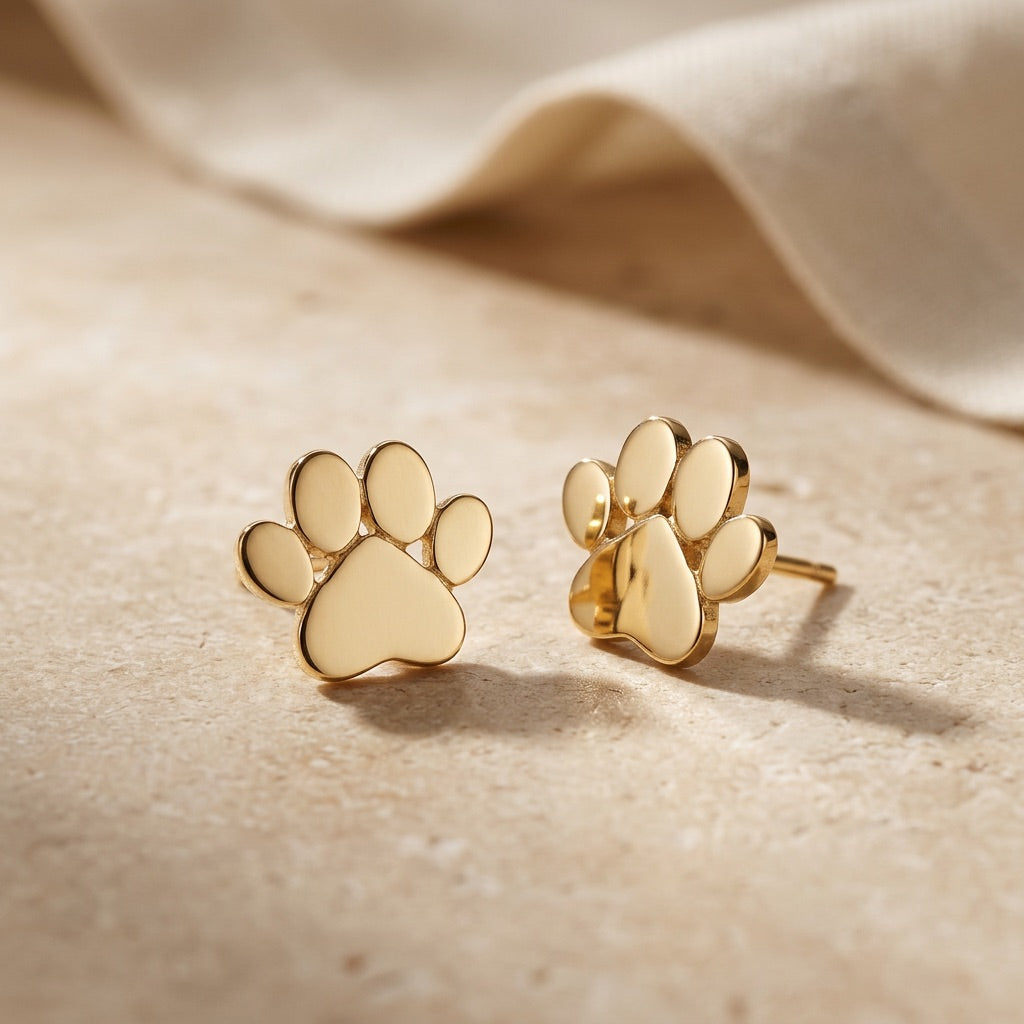 Gold Plated Small Paw Print Stud Earrings on a beige fabric background