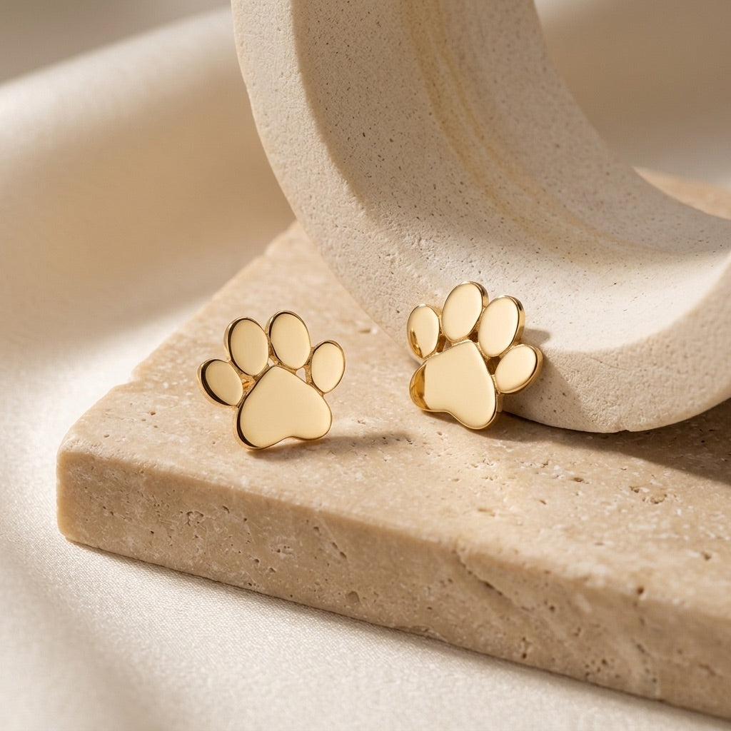 Gold Plated Small Paw Print Stud Earrings on a beige stone surface