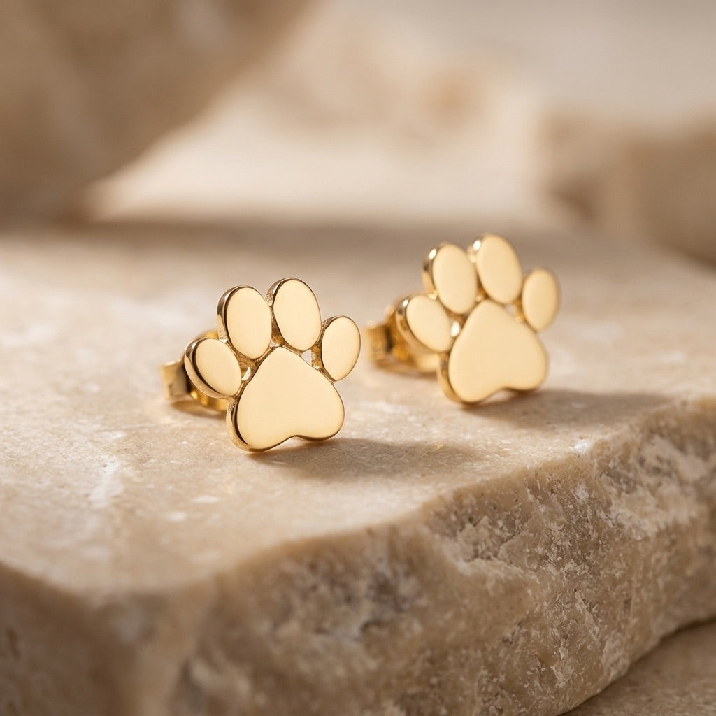 Gold paw print earrings on a stone surface with a blurred background