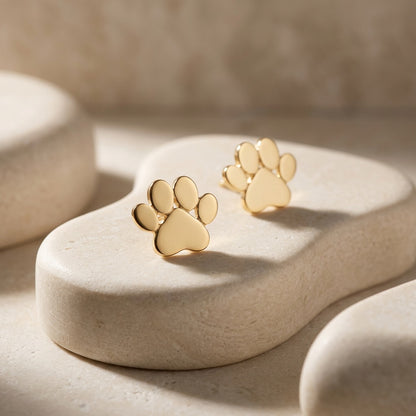 Gold paw print earrings on a beige stone surface