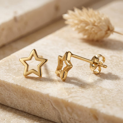 Gold star-shaped earrings on a light stone surface with a natural background