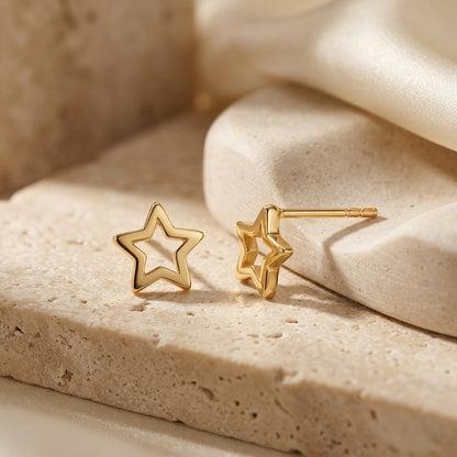 Gold star-shaped earrings on a textured beige surface
