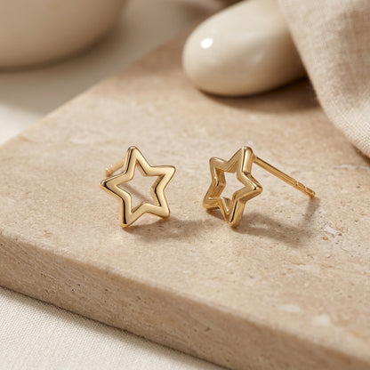 Gold star-shaped earrings on a beige stone surface