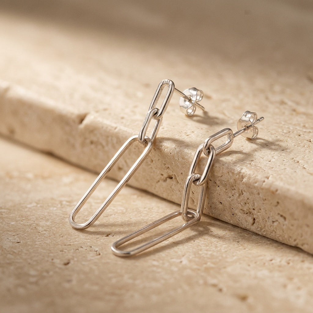 Silver chain earrings on a beige stone surface