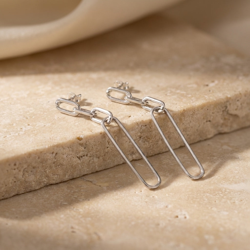 Silver chain earrings on a beige stone surface