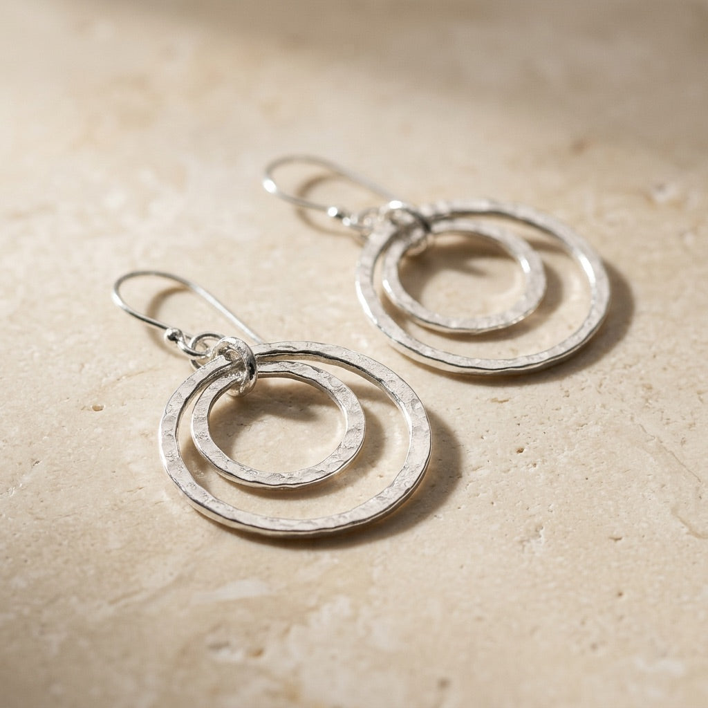 Pair of Double Hammered Circle Drop Earrings on a beige stone surface