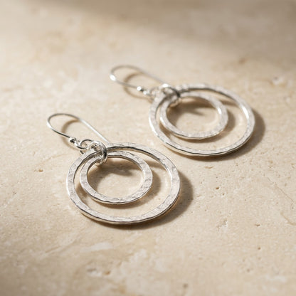 Pair of Double Hammered Circle Drop Earrings on a beige stone surface