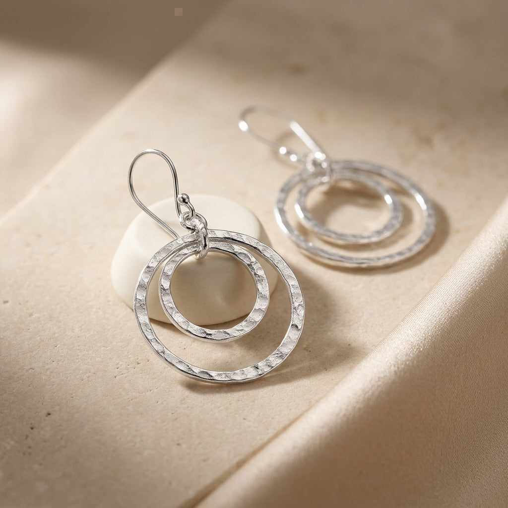 Double Hammered Circle Drop Earrings on a beige fabric background