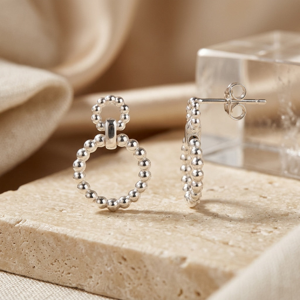 Silver Beaded Circle Link Drop Earrings on a beige stone surface with a soft beige background