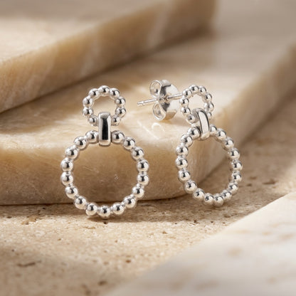 Silver Beaded Circle Link Drop Earrings on a beige stone surface
