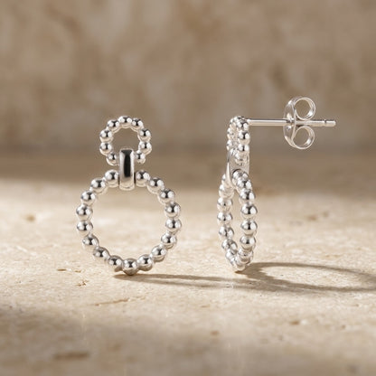Silver Beaded Circle Link Drop Earrings on a stone surface with a blurred background