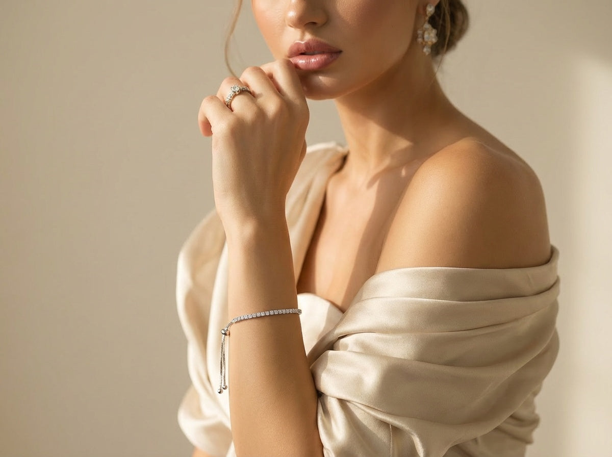 Woman wearing a beige off-shoulder top with jewelry on a neutral background