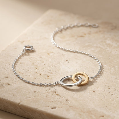 Silver bracelet with gold rings on a beige stone surface