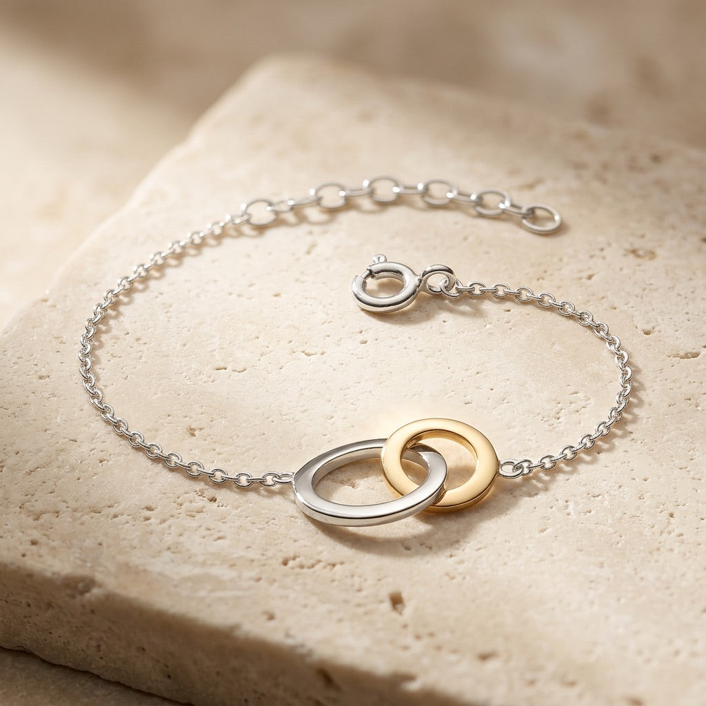 Bracelet with interlocking rings in silver and gold on a beige stone surface