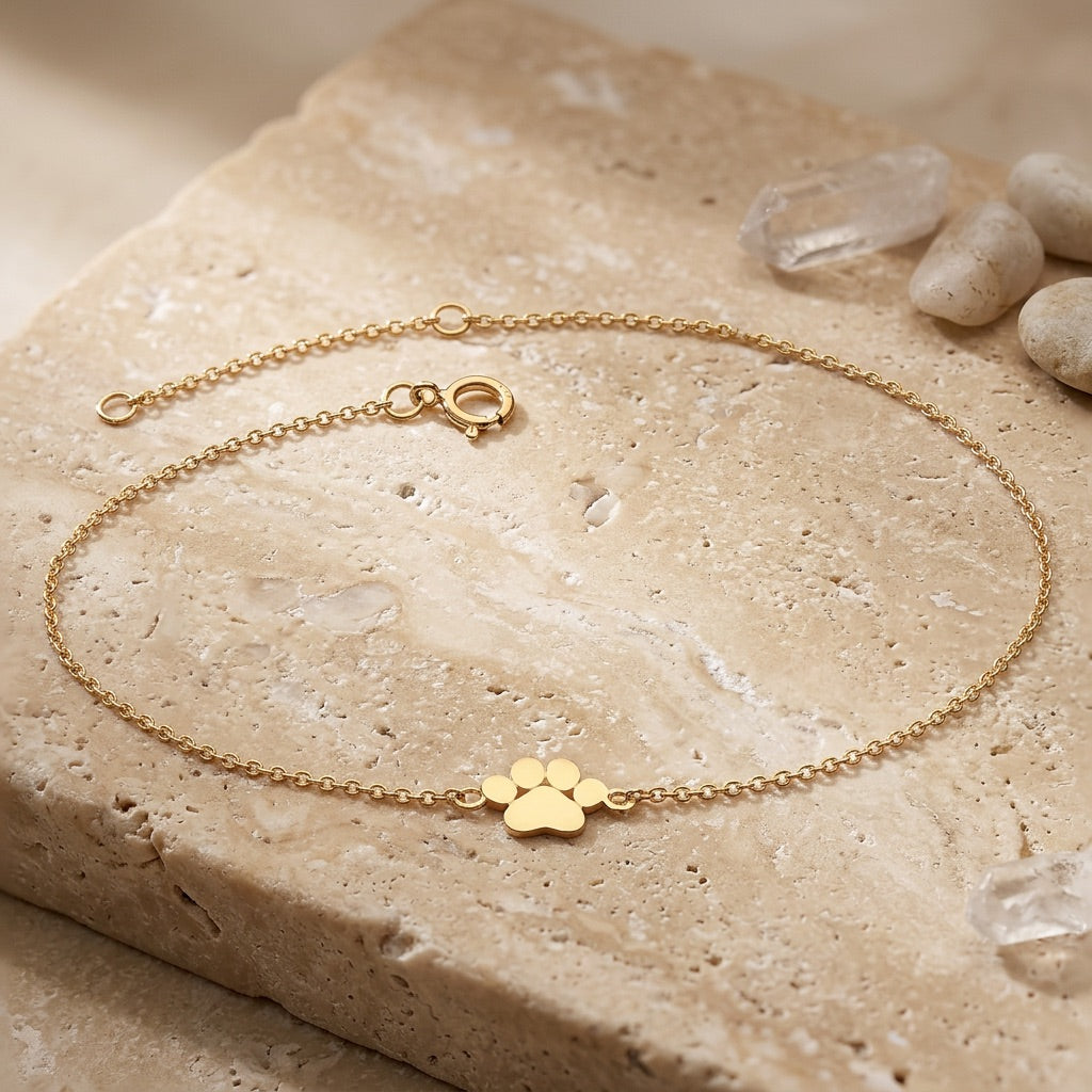 Gold bracelet with paw print charm on a stone surface