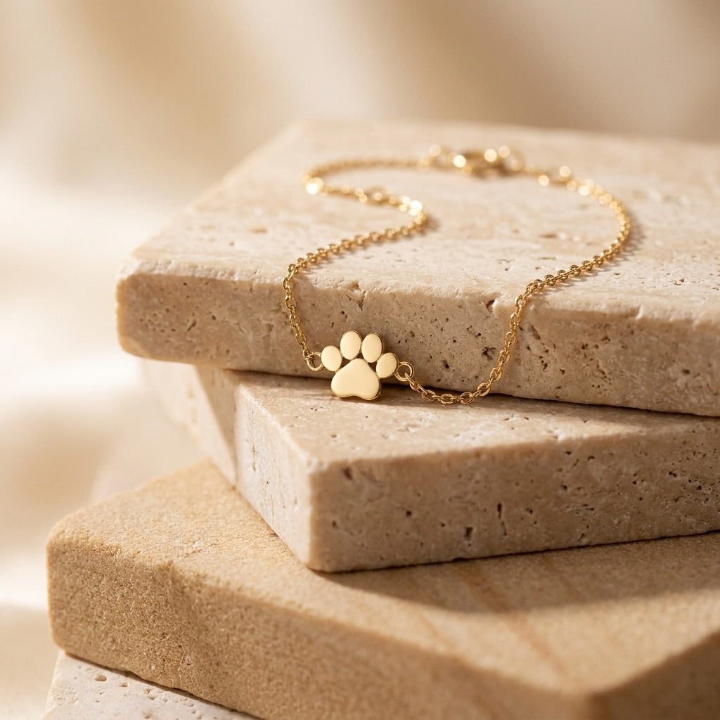 Gold bracelet with paw charm on a textured stone surface