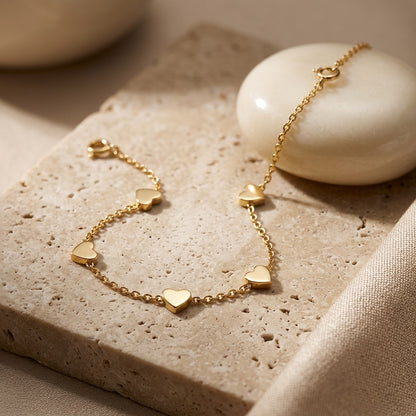 Gold bracelet with heart-shaped charms on a textured surface