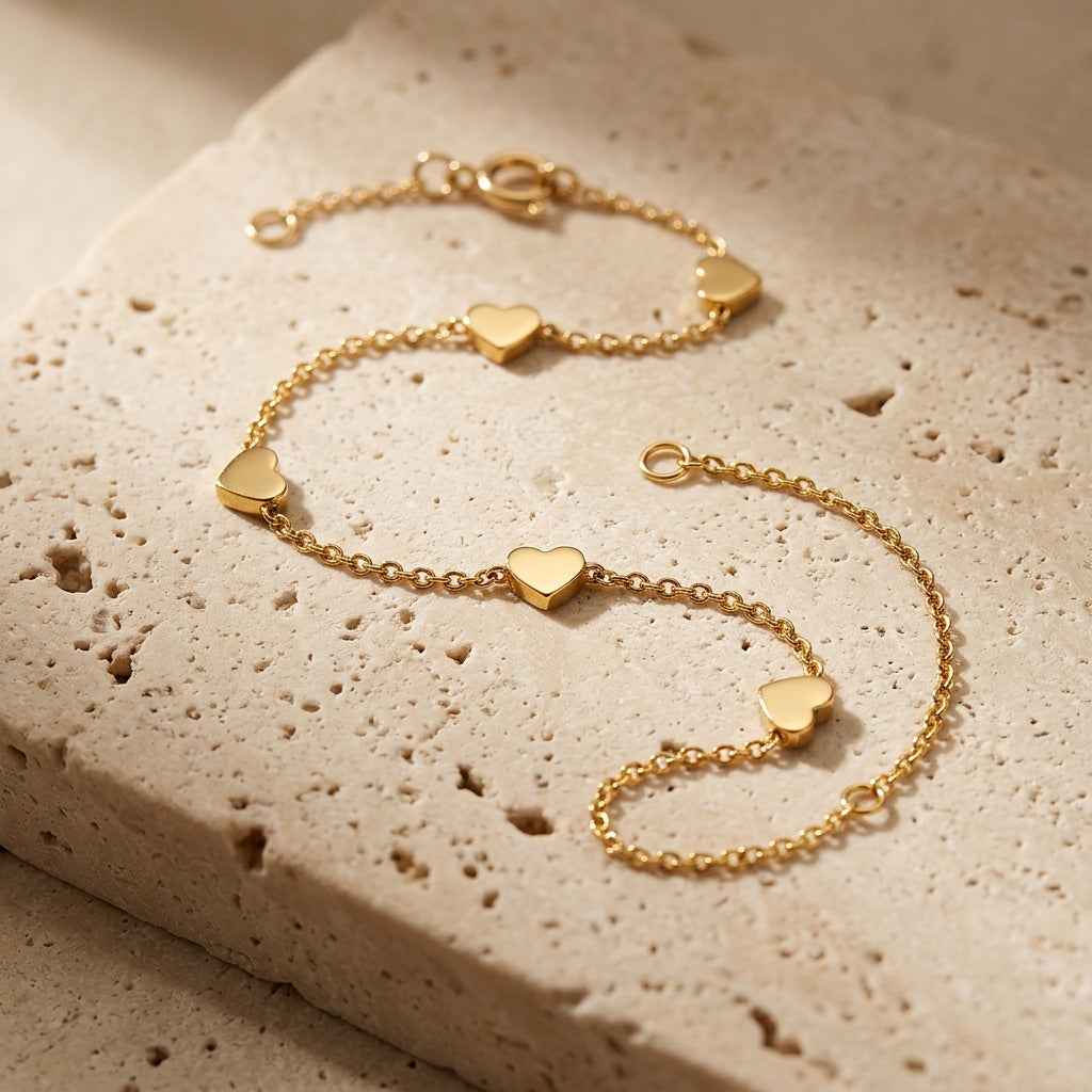 Gold bracelet with heart-shaped charms on a textured beige surface