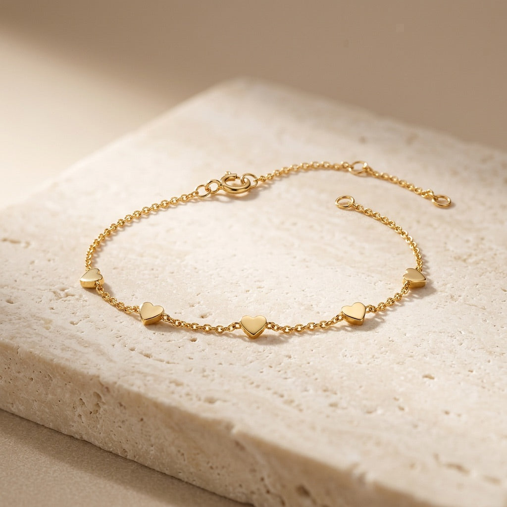 Gold bracelet with heart-shaped charms on a beige stone surface