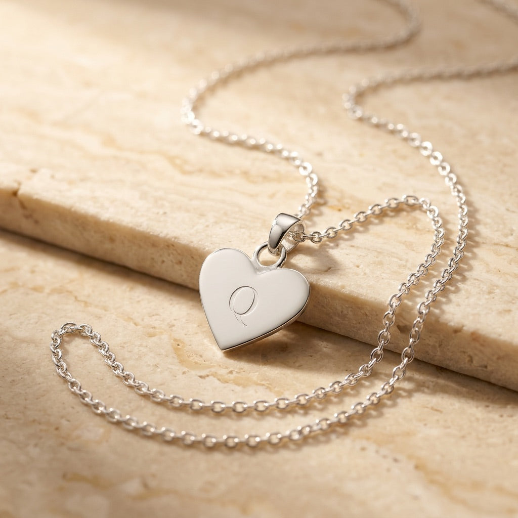 Silver heart-shaped pendant necklace on a beige stone surface